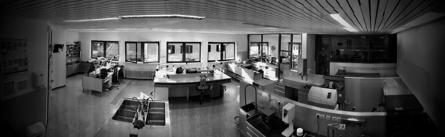 Heller Laborraum mit mehreren Arbeitsplätzen und vielen technischen Geräten zur Fertigung von Zahnersatz.