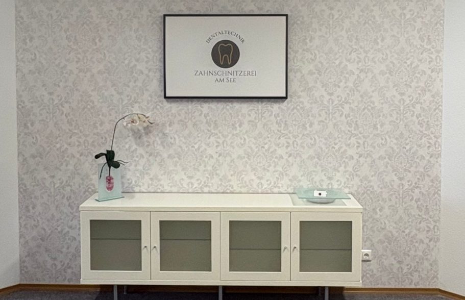 Innenraumansicht mit Sideboard, Blumendekoration, Tapete und Firmenlogo an der Wand